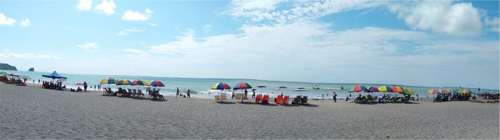 Una amplia escena playera de Atacames con coloridas sombrillas y sillas alineadas cerca del mar. La gente disfruta de diversas actividades bajo un cielo azul parcialmente nublado, creando un ambiente animado y relajado.