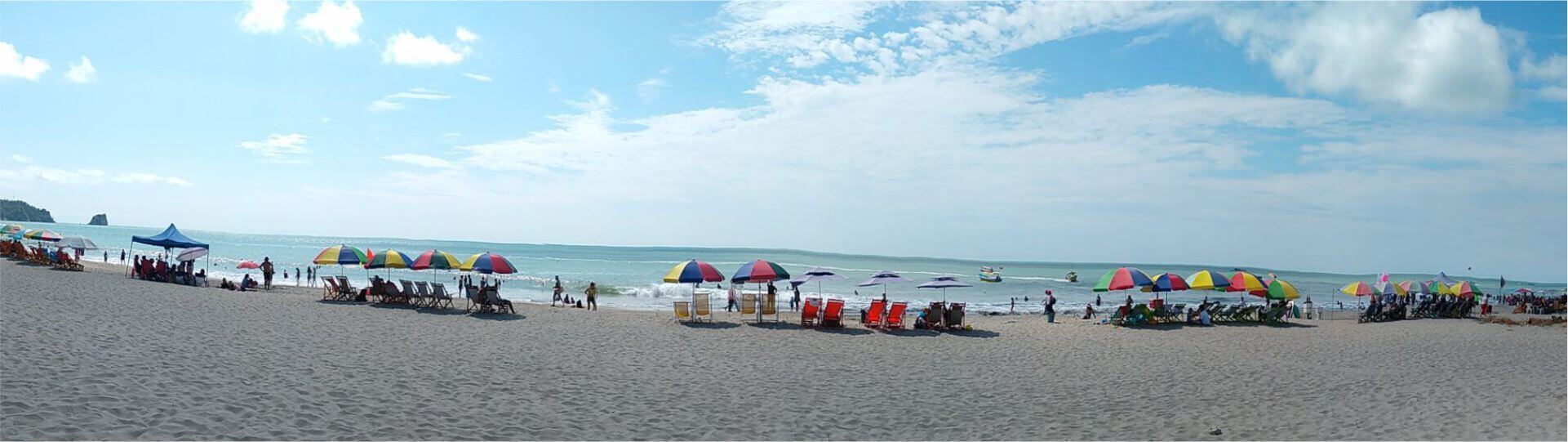 Una amplia escena playera de Atacames con coloridas sombrillas y sillas alineadas cerca del mar. La gente disfruta de diversas actividades bajo un cielo azul parcialmente nublado, creando un ambiente animado y relajado.