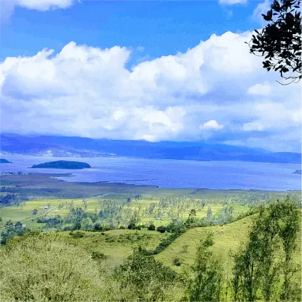 Un paisaje montañoso con La Laguna de la cocha  bajo un cielo azul nublado.